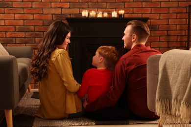 Photo of Happy family spending time together on floor near fireplace at home, back view