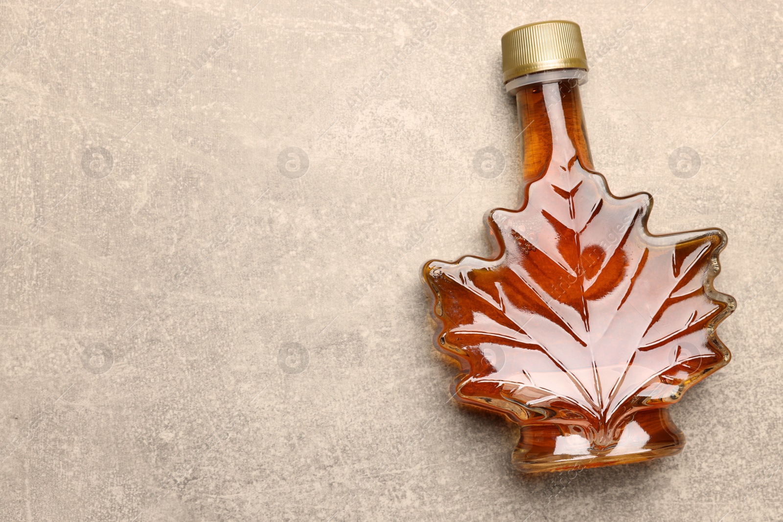 Photo of Leaf shaped bottle of tasty maple syrup on light grey table, top view. Space for text