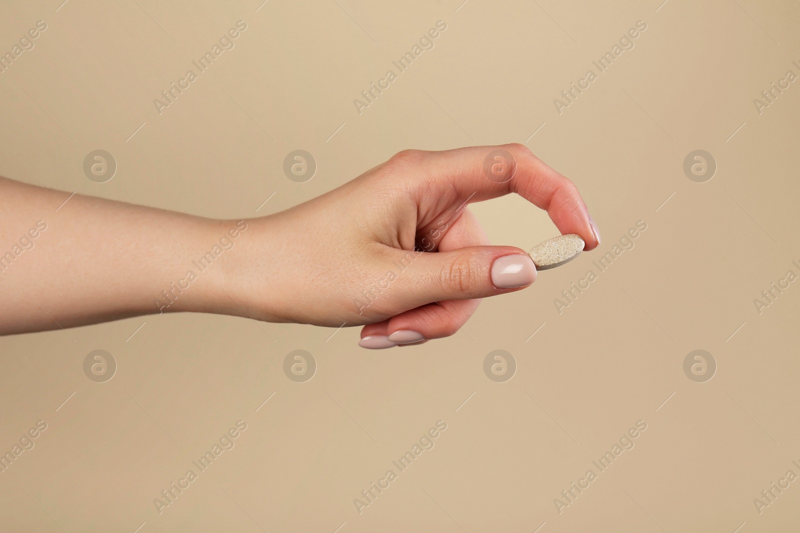 Photo of Woman holding vitamin pill on dark beige background, closeup. Health supplement