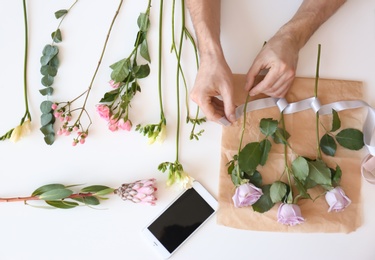 Male florist creating beautiful bouquet at table, top view