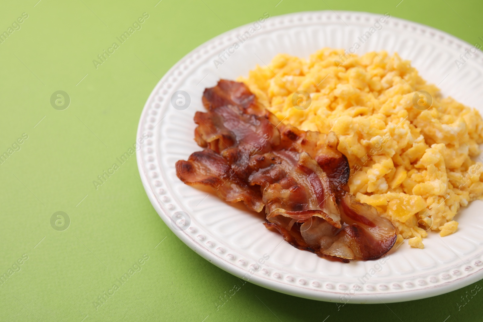 Photo of Delicious scrambled eggs with bacon in plate on light green background, closeup. Space for text