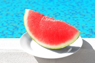 Photo of Slice of fresh juicy watermelon on white plate near swimming pool outdoors