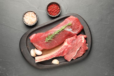 Photo of Pieces of raw beef meat and spices on grey textured table, flat lay