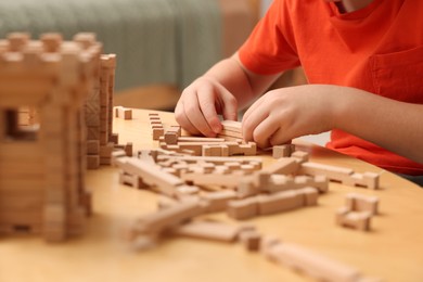 Little boy playing with wooden construction set at table in room, closeup. Child's toy