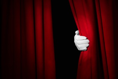 Photo of Person opening red front curtains on black background, closeup