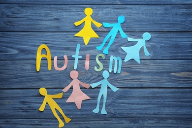 Word "Autism" and paper figures on wooden background