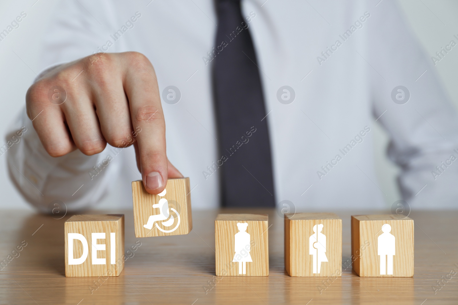 Image of Concept of DEI - Diversity, Equality, Inclusion. Businessman arranging wooden cubes with abbreviation and images of people on table, closeup