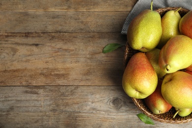 Wicker basket with ripe juicy pears on brown wooden table, top view. Space for text