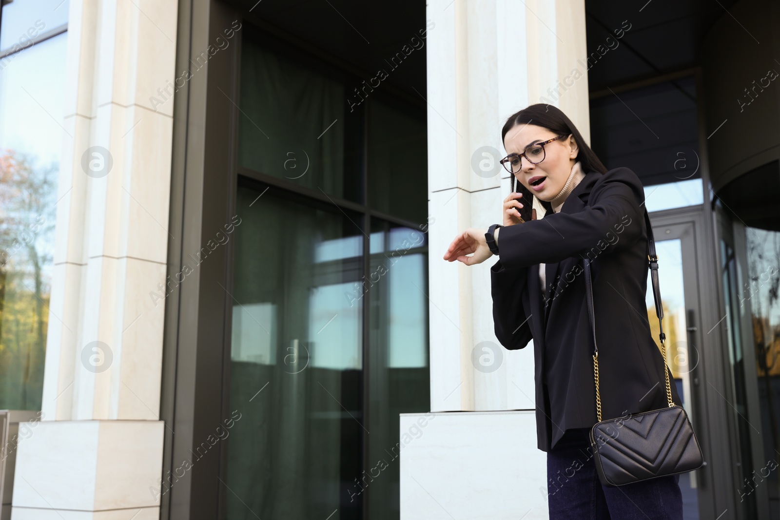 Photo of Emotional woman checking time while talking on smartphone outdoors. Being late concept