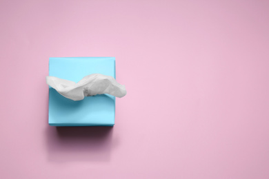 Box with paper tissues on pink background, top view. Space for text