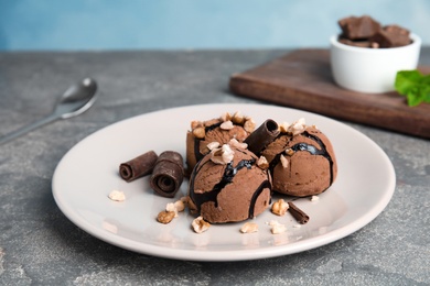 Plate of ice cream with nuts and chocolate curls on grey table. Space for text