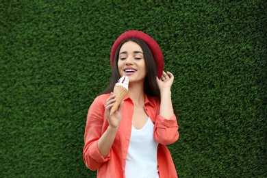Happy young woman with delicious ice cream in waffle cone near grass wall