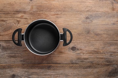 Photo of Empty pot on wooden table, top view. Space for text