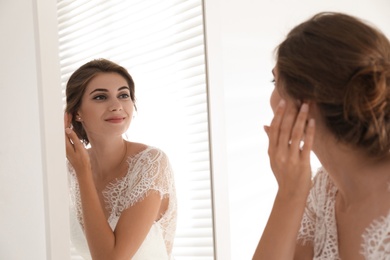 Photo of Young bride in beautiful wedding dress near mirror indoors