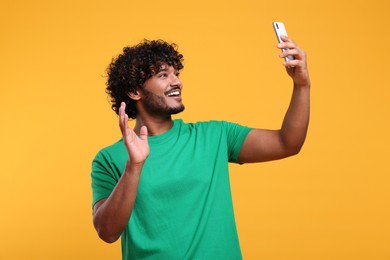 Photo of Handsome smiling man having video call via smartphone on yellow background