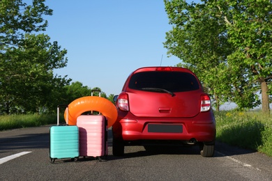 Color suitcases and inflatable ring near family car on highway. Summer vacation