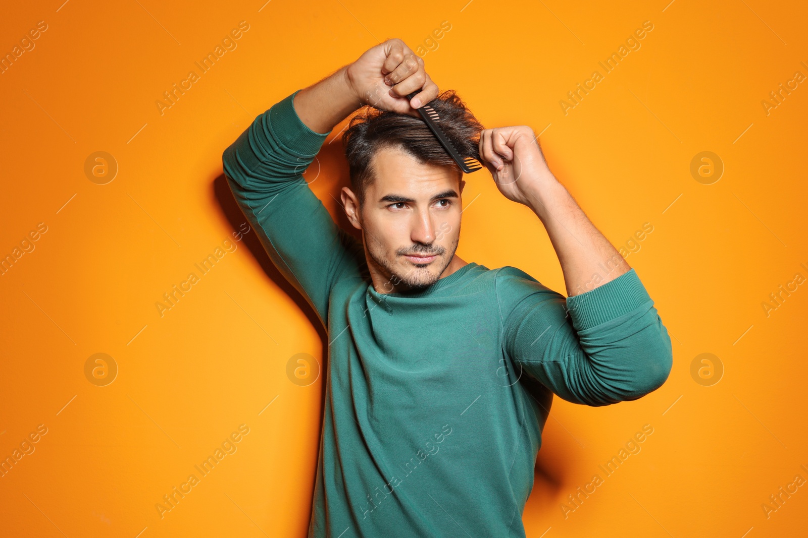 Photo of Young man with comb posing on color background. Trendy hairstyle