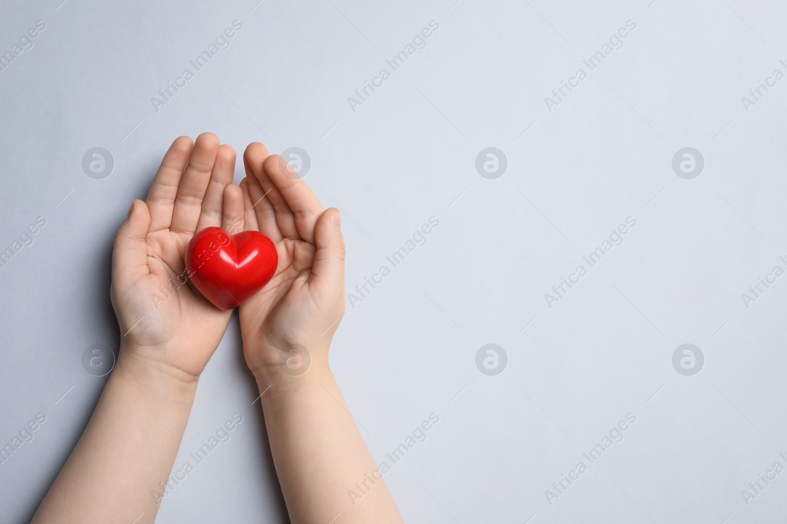 Photo of Child holding red heart on light grey background, top view. Space for text