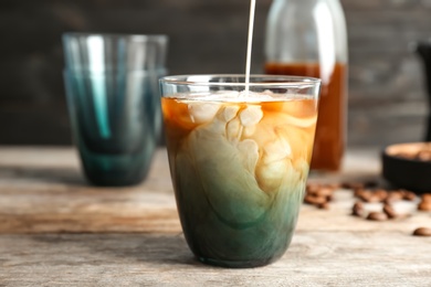 Pouring milk into glass with cold brew coffee on table