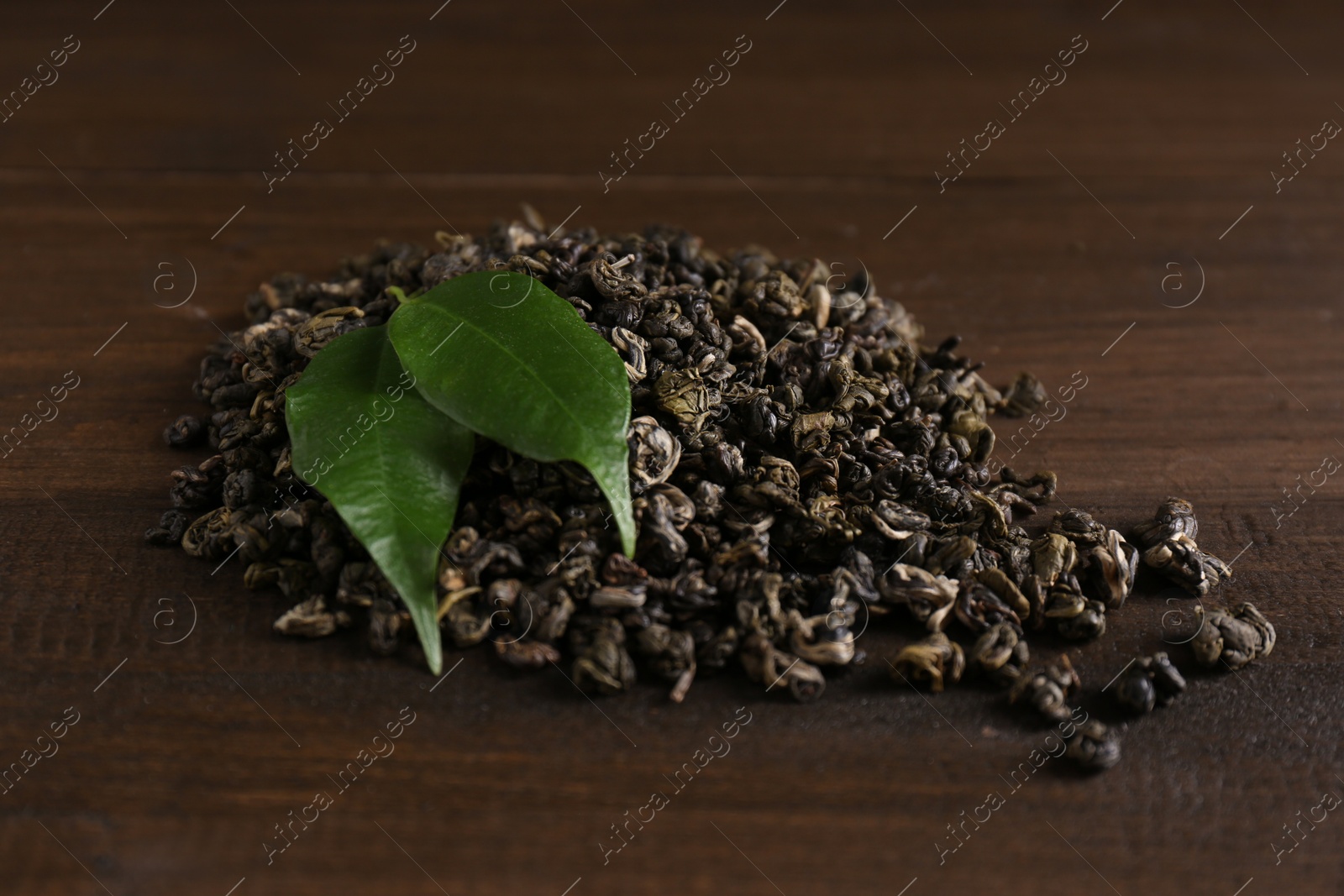 Photo of Heap of dried green tea leaves on wooden table, closeup