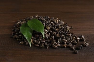 Photo of Heap of dried green tea leaves on wooden table, closeup