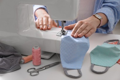 Photo of Woman making cloth mask with sewing machine at white table, closeup