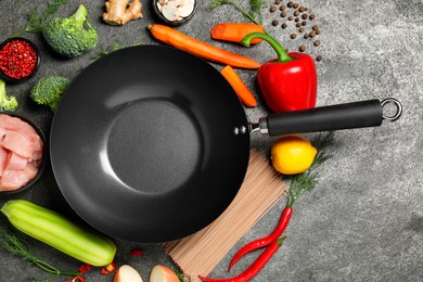 Photo of Empty iron wok surrounded by raw ingredients on grey table, flat lay