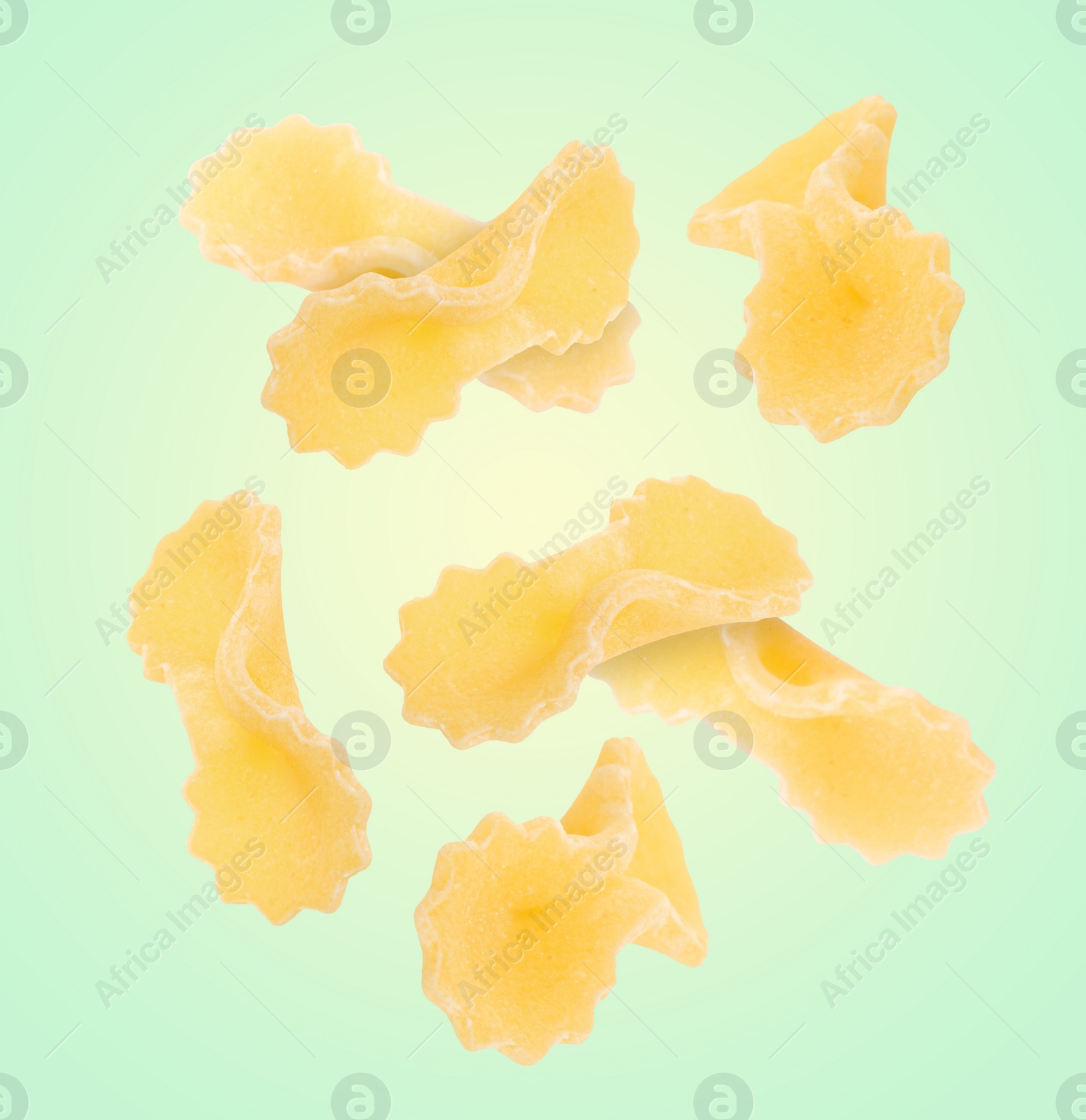 Image of Raw farfalline pasta falling on light green background