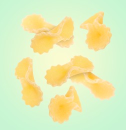 Raw farfalline pasta falling on light green background