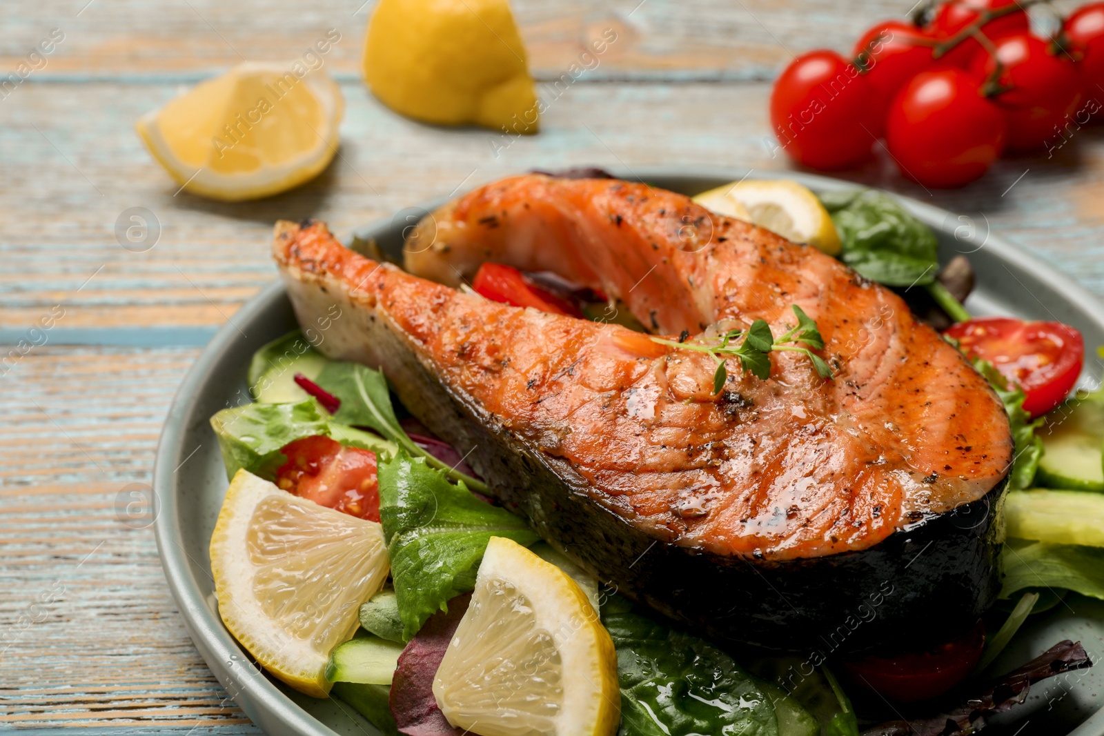 Photo of Tasty salmon steak with lemon and vegetables on white wooden table, closeup