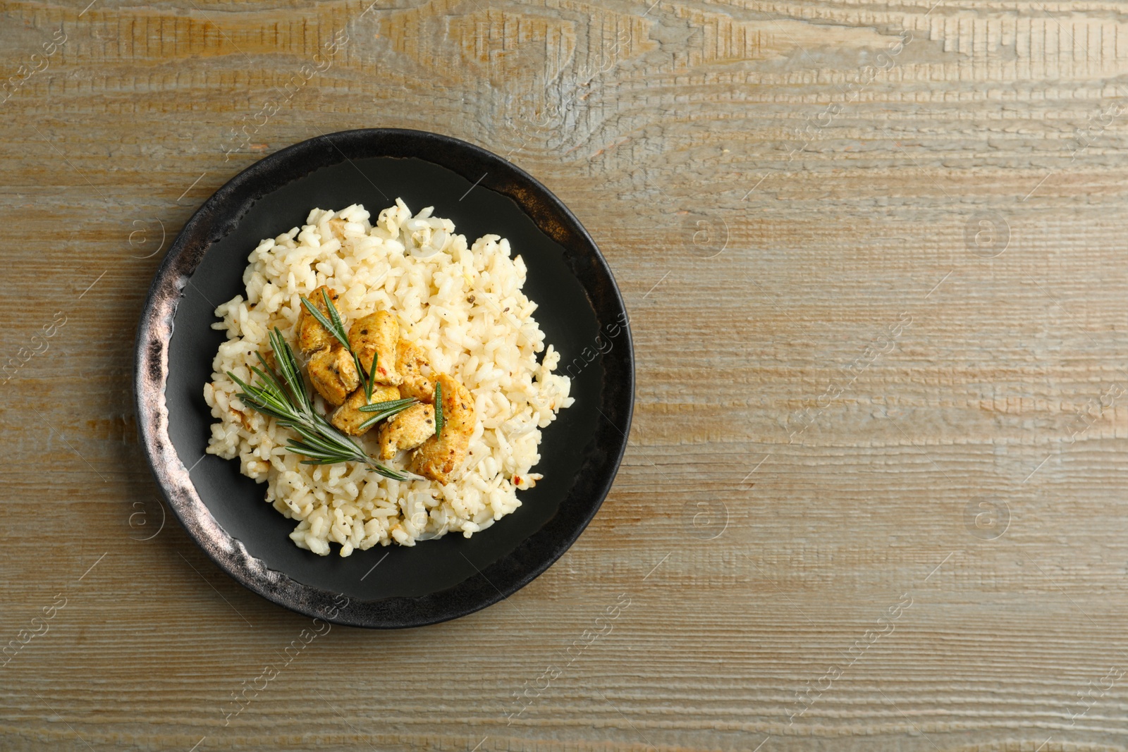Photo of Delicious risotto with chicken on wooden table, top view. Space for text