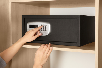Photo of Woman opening black steel safe with electronic lock at hotel, closeup