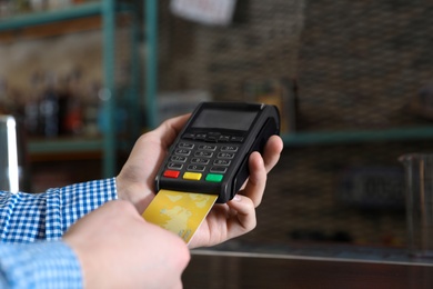 Man using credit card machine for non cash payment in cafe, closeup. Space for text