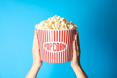 Photo of Woman holding popcorn bucket on color background, closeup. Cinema snack