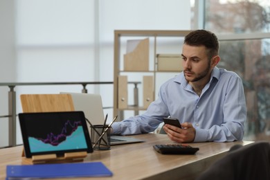 Photo of Forex trader with smartphone working in office