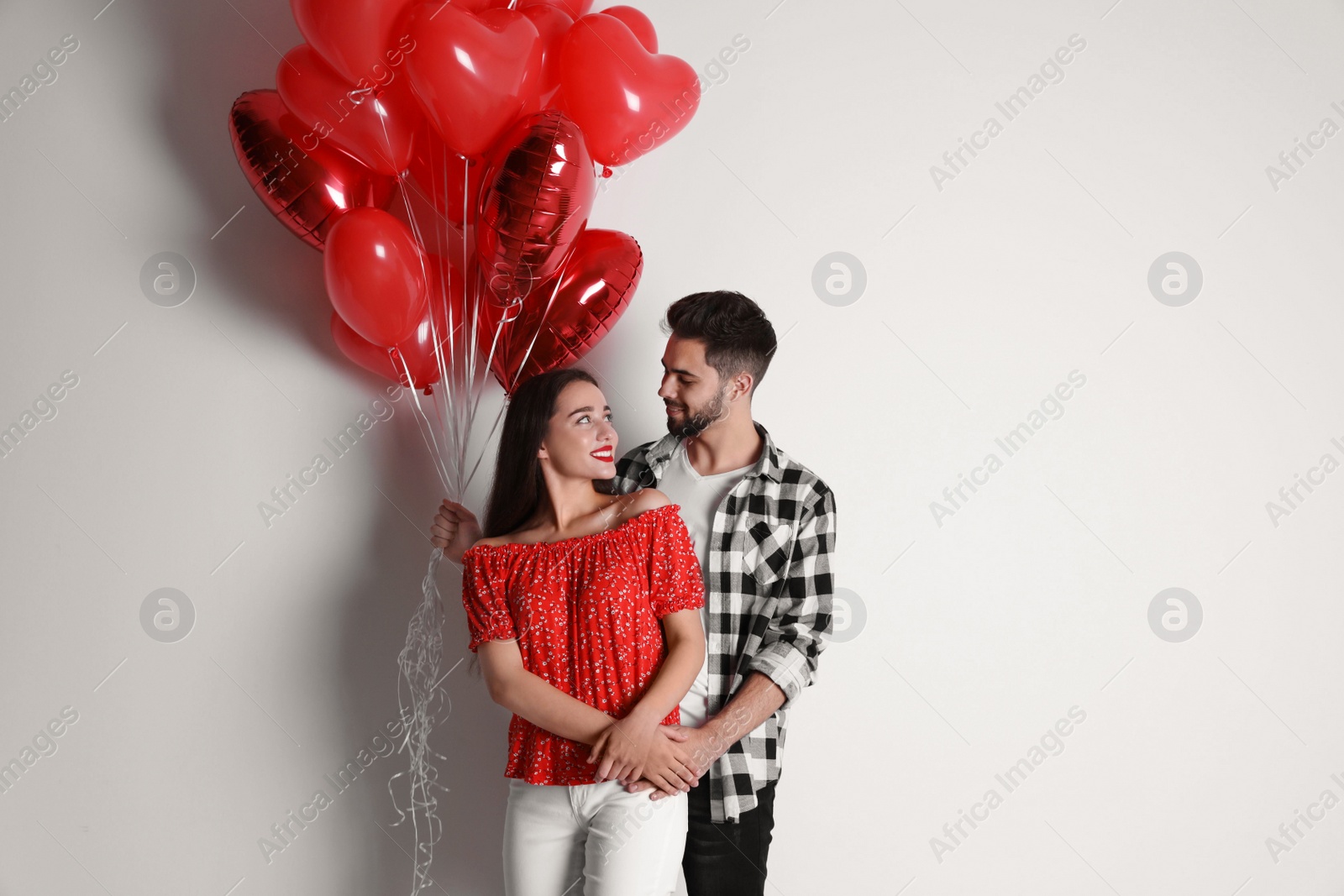 Photo of Happy young couple with heart shaped balloons on light background. Valentine's day celebration