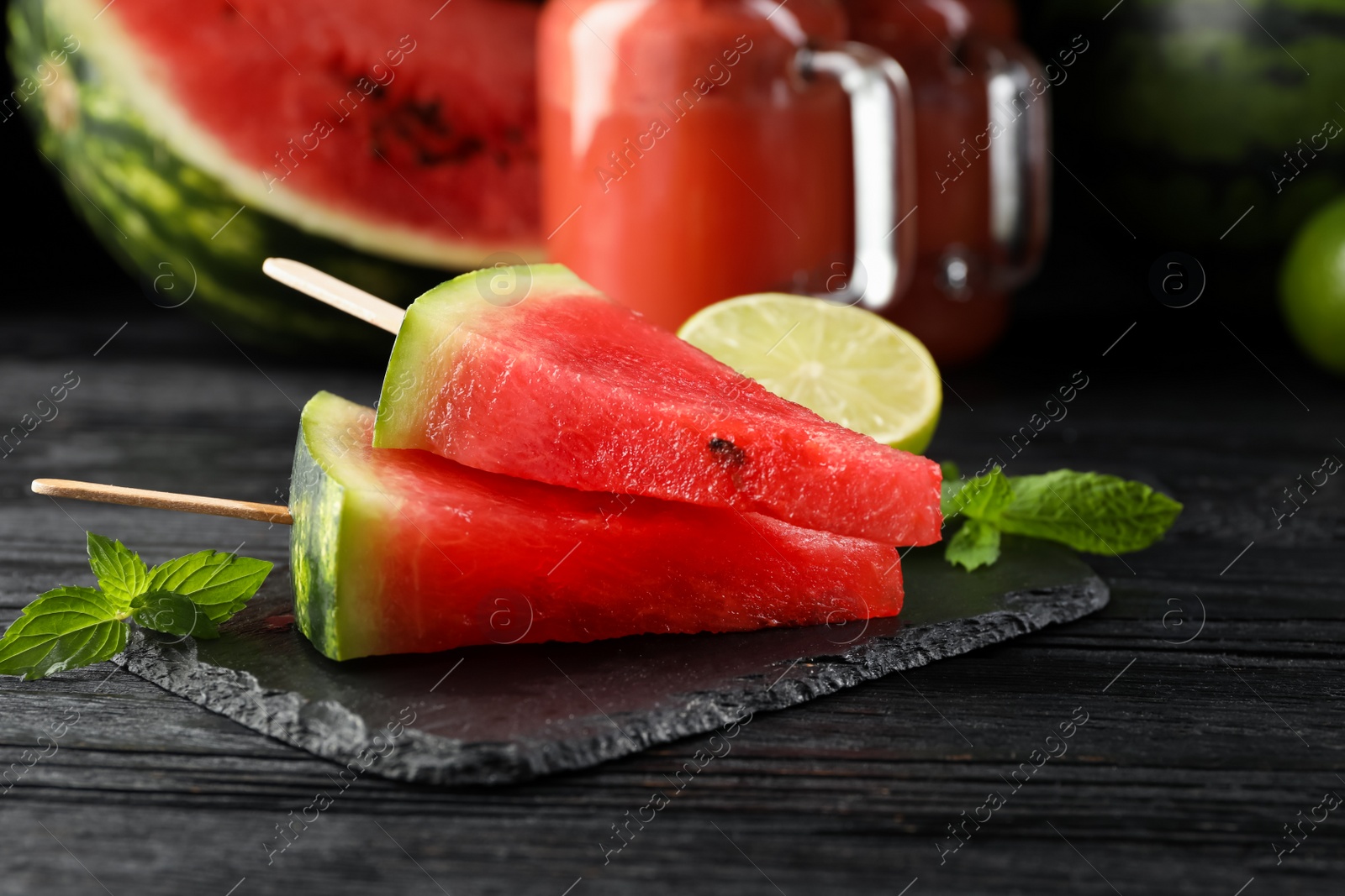 Photo of Slate board with cut juicy watermelon and lime on black wooden table