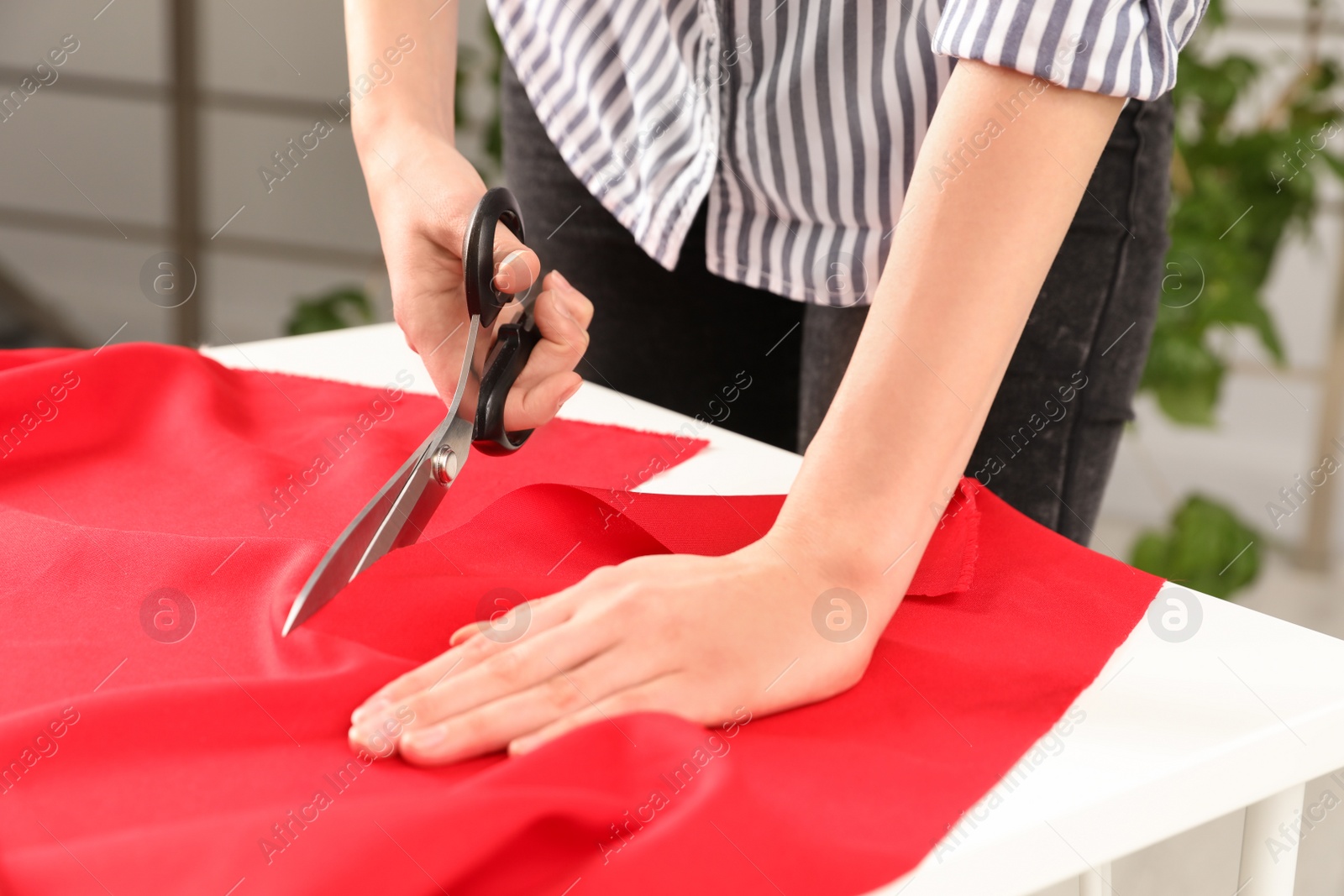 Photo of Woman cutting fabric with sharp scissors at table indoors, closeup