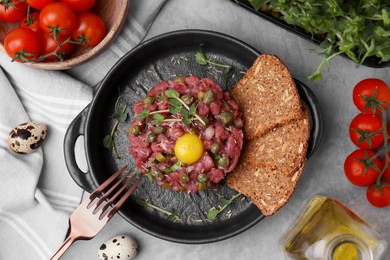 Photo of Tasty beef steak tartare served with yolk, capers and bread on light grey table, flat lay