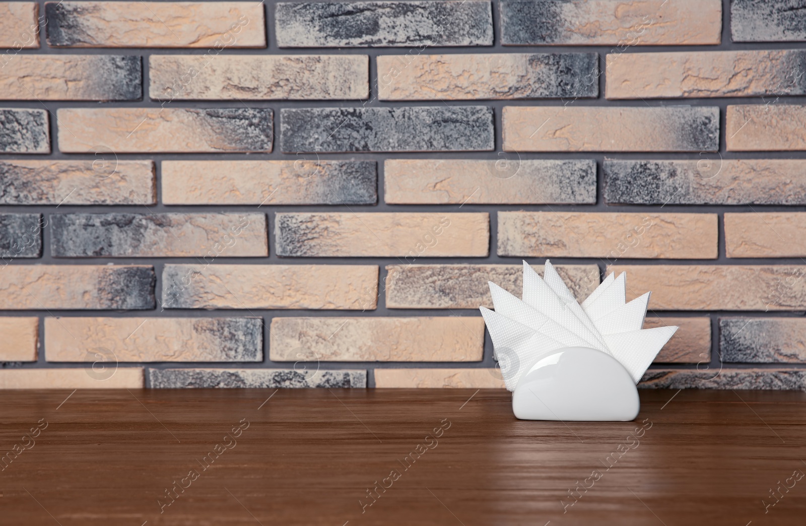 Photo of Napkin holder with paper serviettes on table against brick wall. Space for text