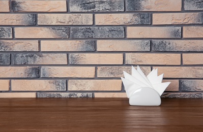 Photo of Napkin holder with paper serviettes on table against brick wall. Space for text