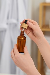 Photo of Woman with bottle of essential oil on blurred background, closeup