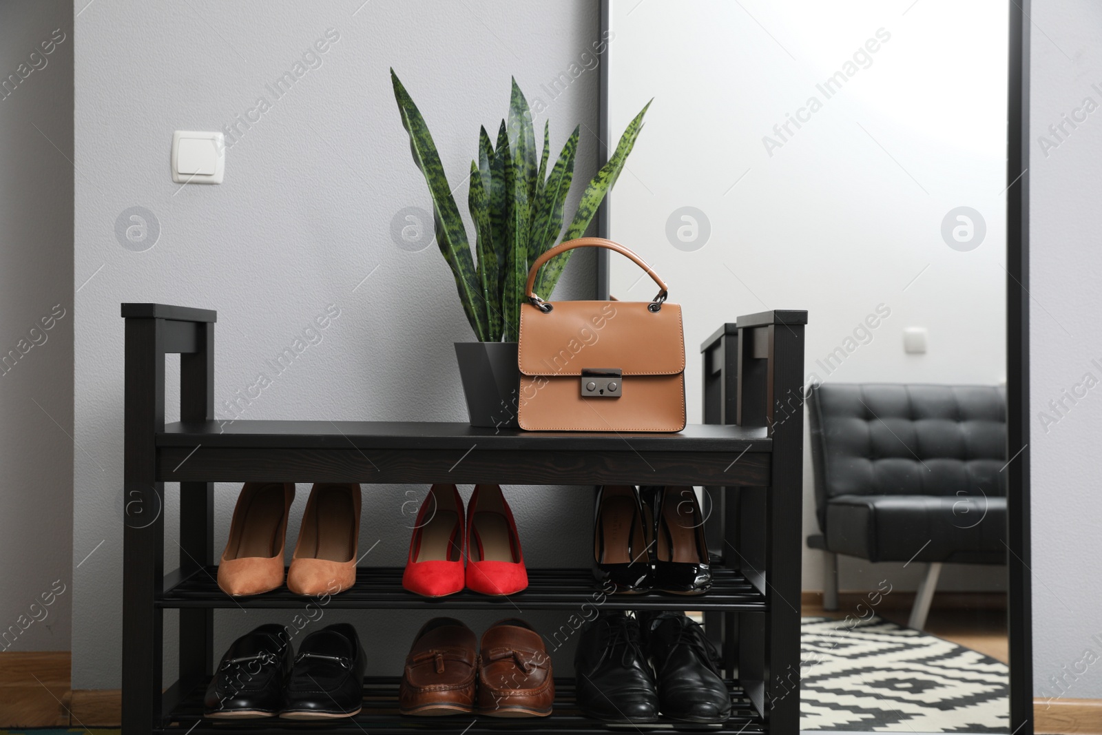 Photo of Shelving unit with stylish shoes and large mirror near grey wall in hallway