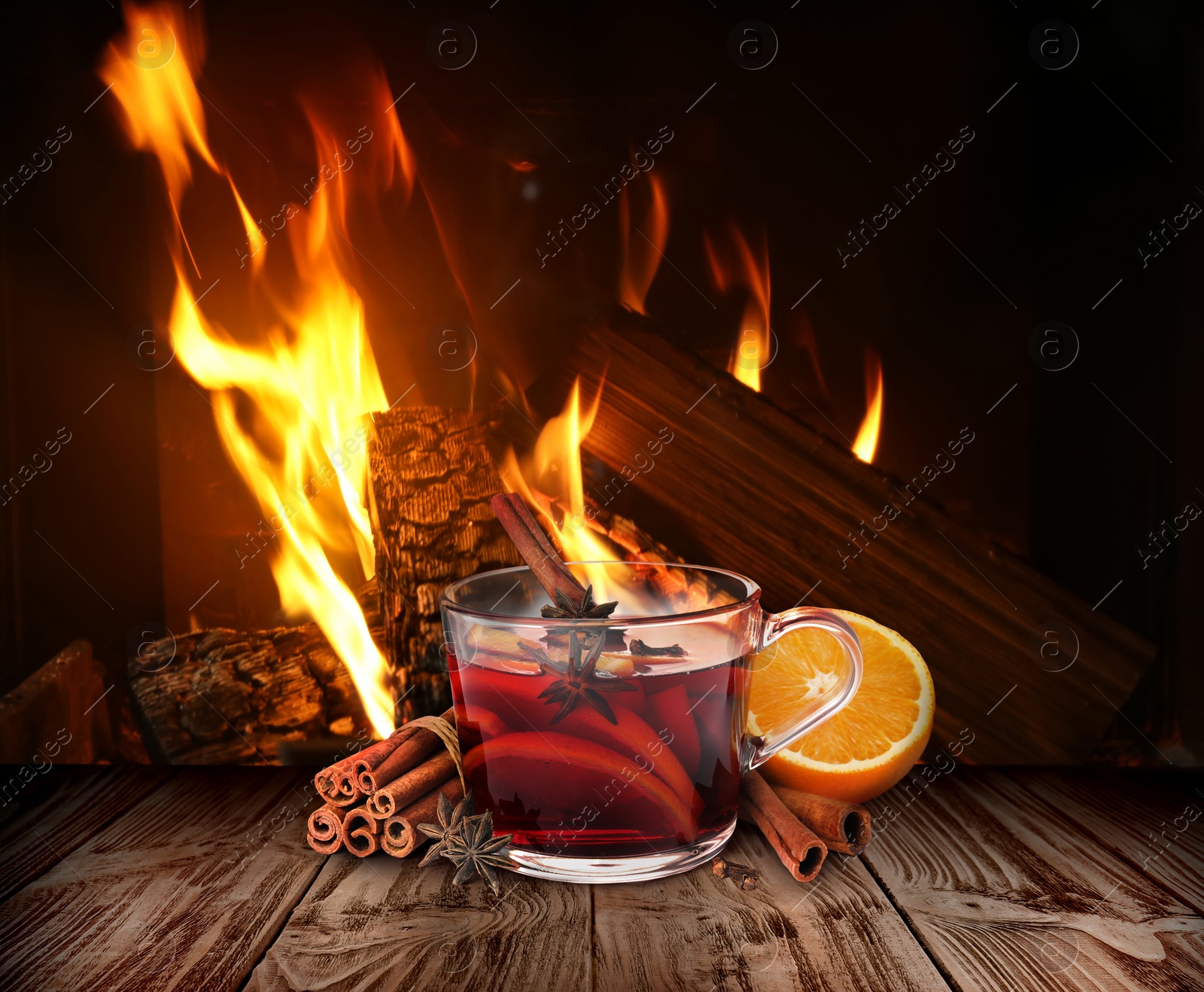 Image of Mulled wine in glass cup on wooden table near fireplace