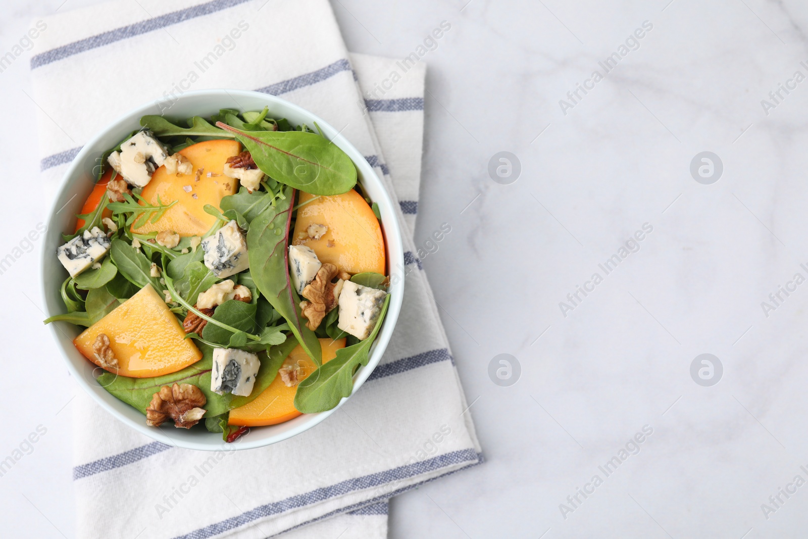 Photo of Tasty salad with persimmon, blue cheese and walnuts served on white marble table, top view. Space for text