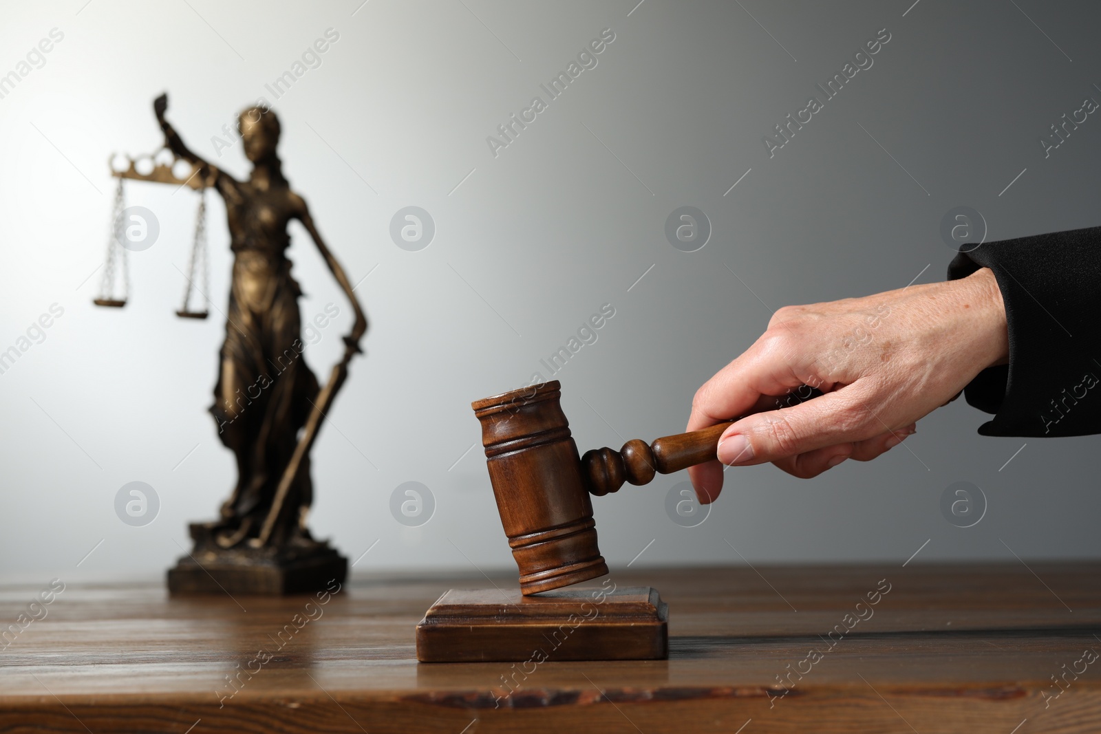 Photo of Judge striking mallet at wooden table against grey background, closeup. Space for text