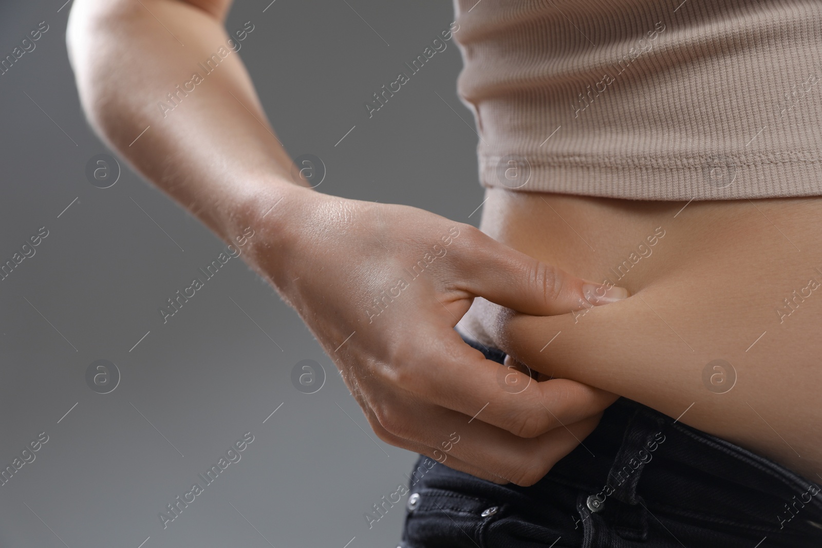 Photo of Woman touching belly fat on grey background, closeup. Overweight problem