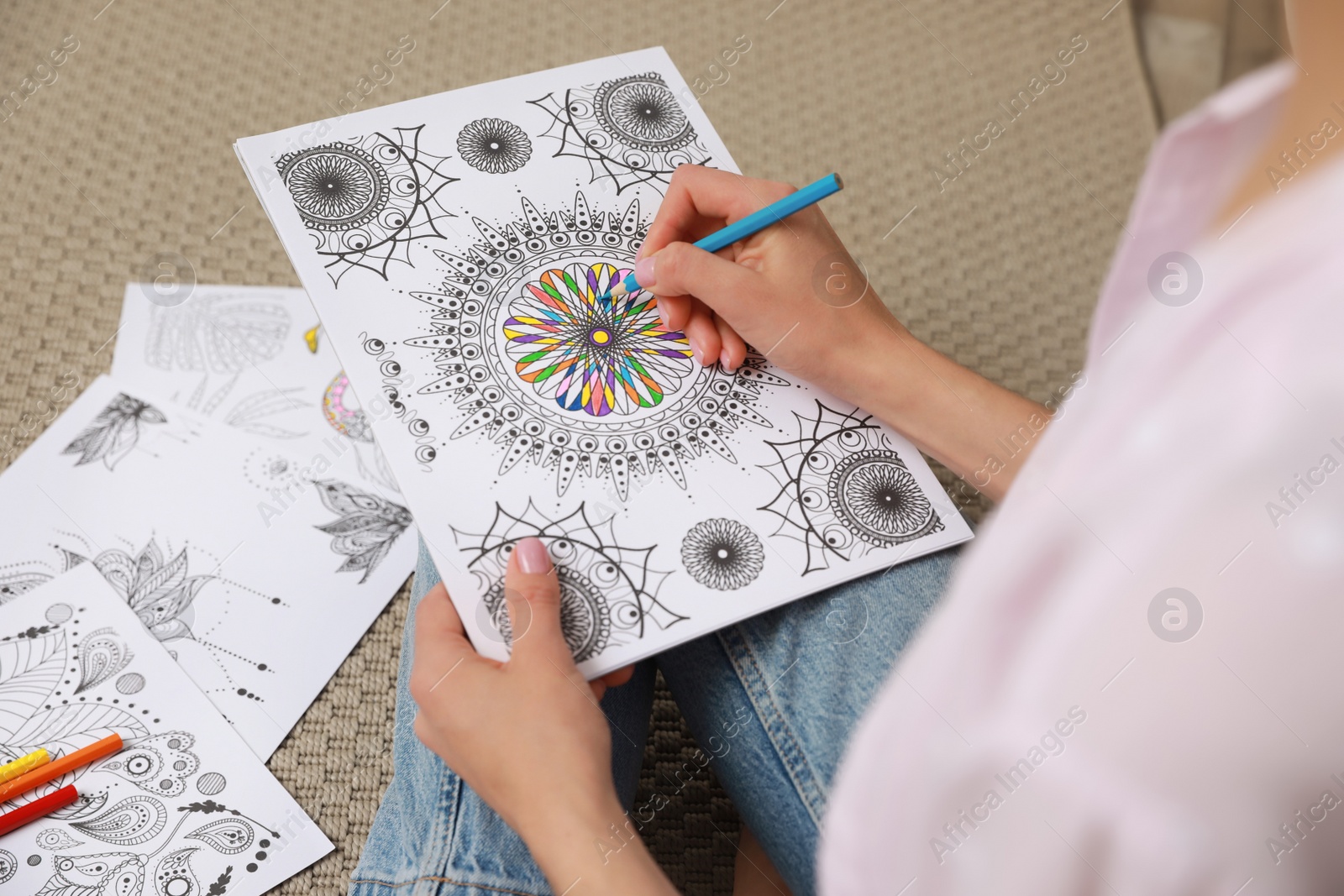 Photo of Young woman coloring antistress page on floor, closeup