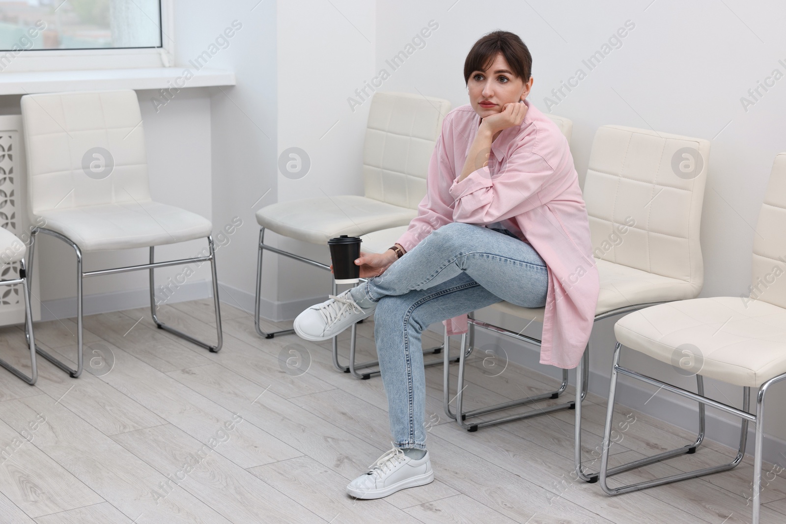 Photo of Woman with cup of drink waiting for appointment indoors