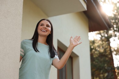 Photo of Neighbor greeting. Happy young woman waving near house outdoors, low angle view